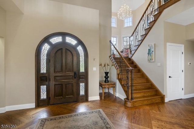 foyer entrance featuring a chandelier, baseboards, stairway, a towering ceiling, and arched walkways