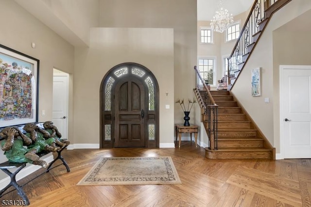 entryway with a towering ceiling, stairway, a chandelier, and baseboards