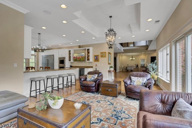 living area featuring a chandelier, beverage cooler, wood finished floors, recessed lighting, and ornamental molding
