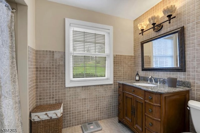full bath with tile walls, toilet, vanity, wainscoting, and tile patterned floors