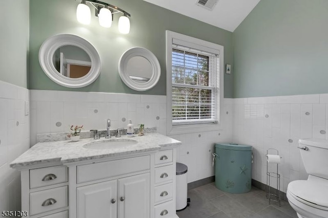 bathroom featuring toilet, tile walls, wainscoting, tile patterned flooring, and vanity