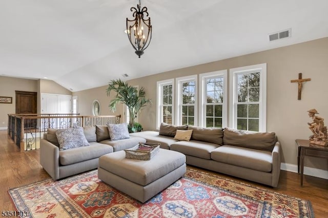 living area featuring lofted ceiling, wood finished floors, baseboards, and a chandelier