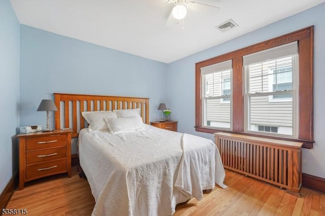 bedroom featuring radiator, light wood finished floors, baseboards, and ceiling fan