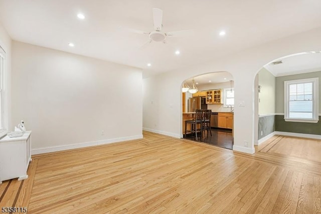 unfurnished living room featuring arched walkways, light wood-type flooring, plenty of natural light, a ceiling fan, and recessed lighting