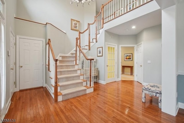 foyer entrance featuring wood finished floors, a towering ceiling, stairway, baseboards, and a chandelier