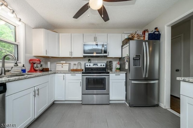 kitchen featuring appliances with stainless steel finishes, a sink, tasteful backsplash, a textured ceiling, and ceiling fan