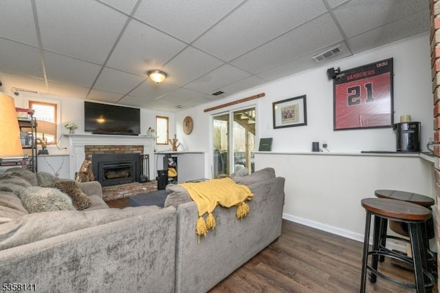 living area featuring a paneled ceiling, a fireplace, wood finished floors, and baseboards
