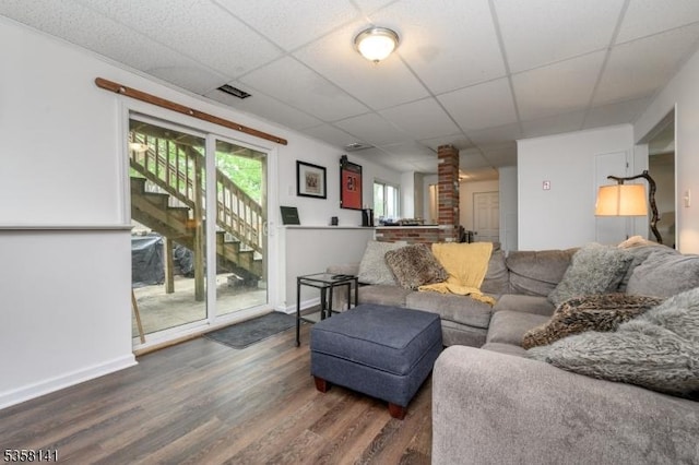 living area featuring wood finished floors, a drop ceiling, baseboards, and stairway