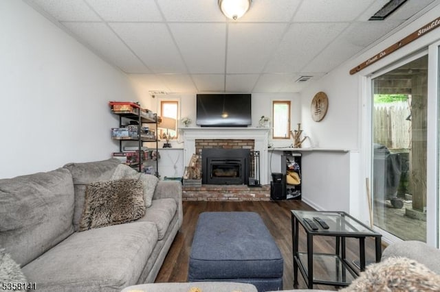 living room featuring wood finished floors, a brick fireplace, a paneled ceiling, and plenty of natural light