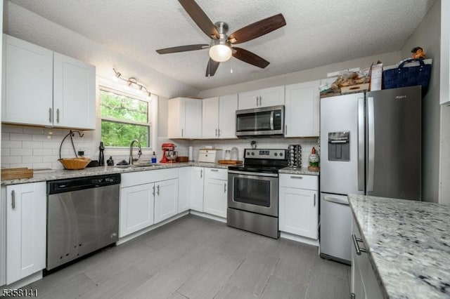 kitchen with stainless steel appliances, a sink, a ceiling fan, tasteful backsplash, and a textured ceiling
