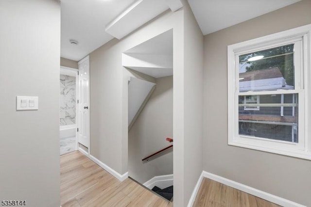 corridor with an upstairs landing, wood finished floors, and baseboards
