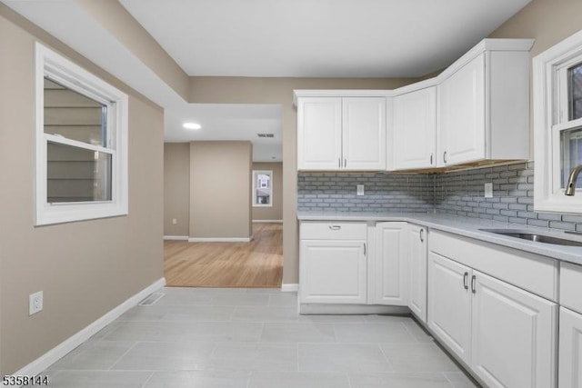 kitchen featuring a sink, baseboards, light countertops, and tasteful backsplash