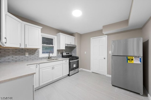 kitchen with stainless steel appliances, a sink, backsplash, under cabinet range hood, and white cabinetry