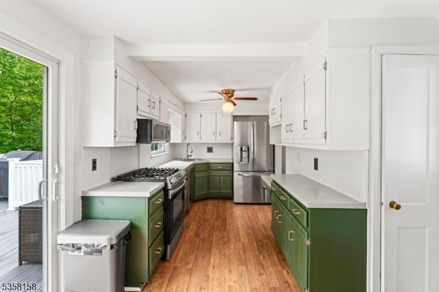 kitchen with green cabinetry, appliances with stainless steel finishes, a sink, white cabinets, and light countertops