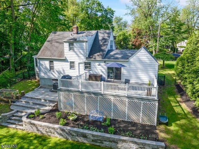 back of house with a wooden deck, a chimney, view of wooded area, and a shingled roof