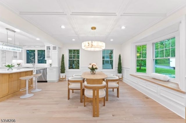 dining room featuring a chandelier, coffered ceiling, healthy amount of natural light, light wood-style floors, and a decorative wall