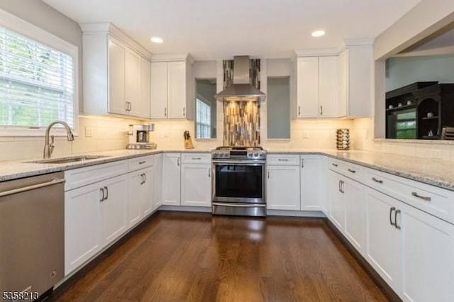 kitchen with wall chimney range hood, stainless steel appliances, a sink, backsplash, and white cabinetry