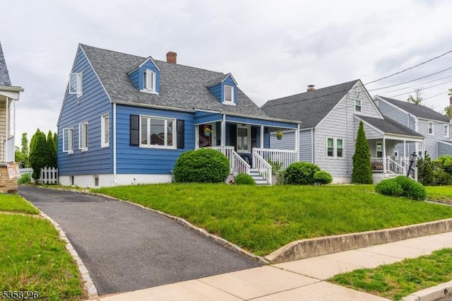 new england style home with a porch, a front lawn, a chimney, and roof with shingles