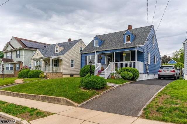 new england style home with a porch, a front lawn, and a chimney