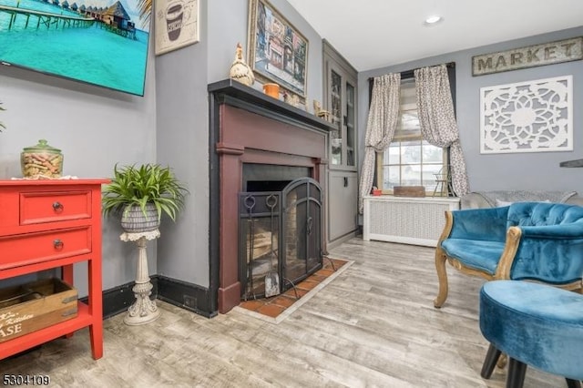 living area with a fireplace with flush hearth, wood finished floors, radiator, and recessed lighting