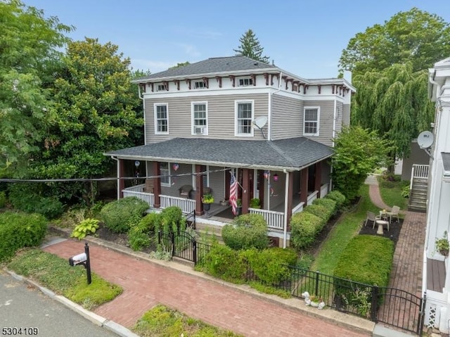 italianate-style house with covered porch, a fenced front yard, and a shingled roof