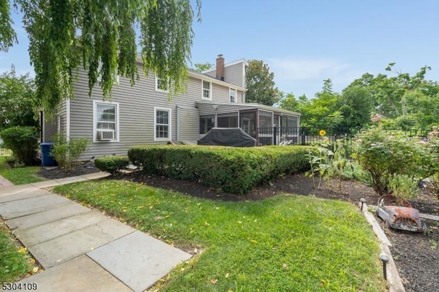 rear view of house with a sunroom, a chimney, and a yard