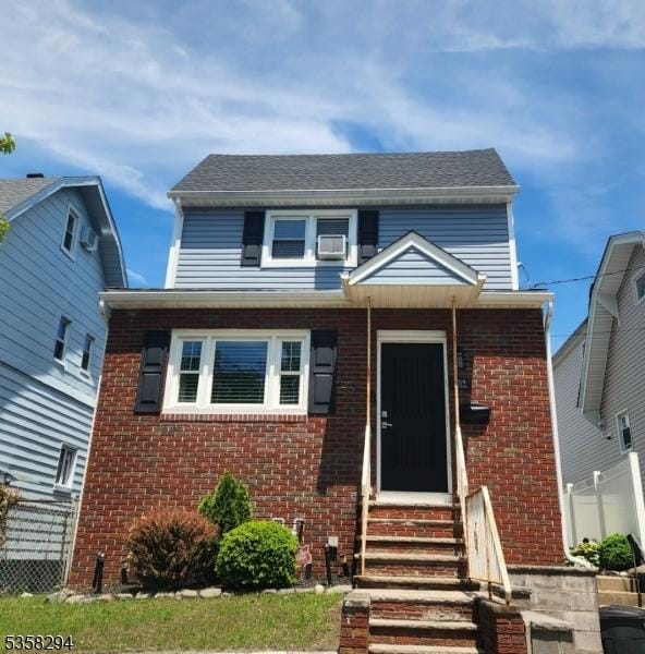 view of front of house with entry steps, brick siding, and fence