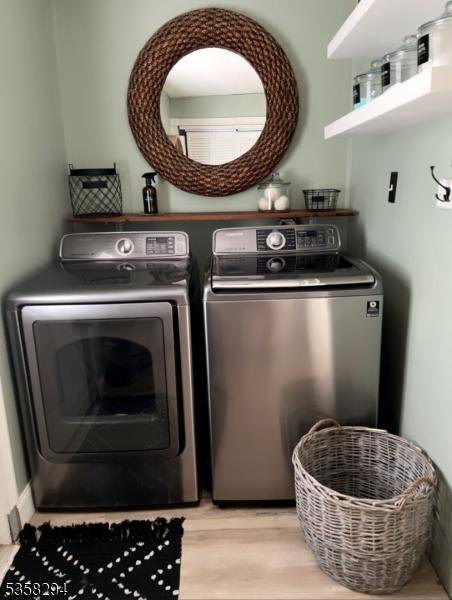 clothes washing area featuring washer and clothes dryer and light wood finished floors