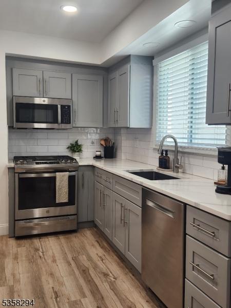kitchen with stainless steel appliances, gray cabinets, a sink, decorative backsplash, and recessed lighting