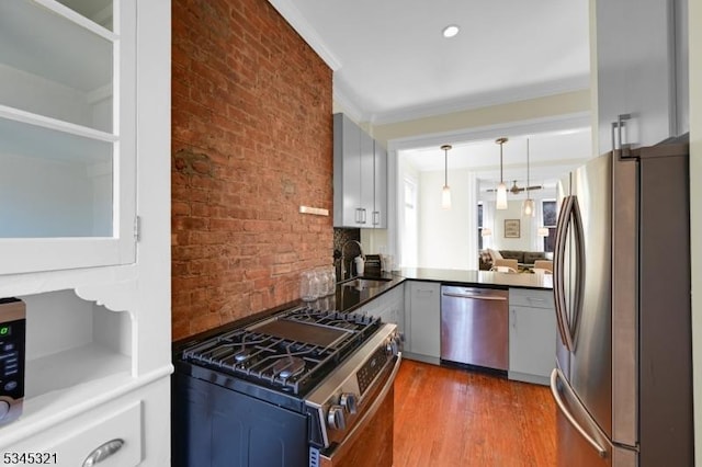 kitchen featuring stainless steel appliances, a sink, dark wood-style flooring, brick wall, and pendant lighting