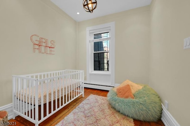 bedroom featuring wood finished floors, baseboard heating, and baseboards