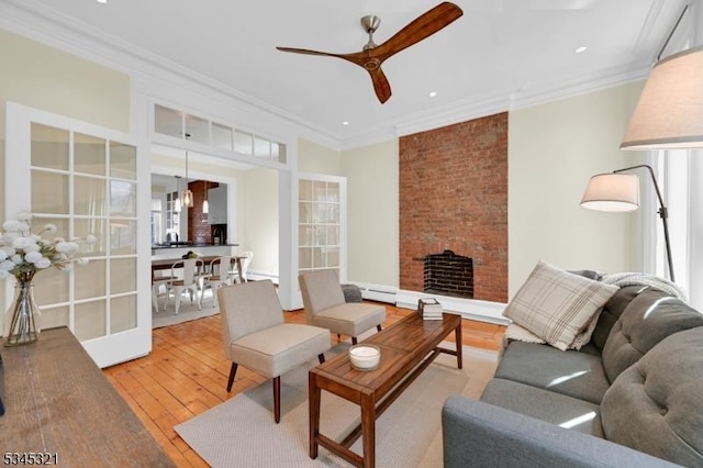 living area featuring ceiling fan, wood-type flooring, crown molding, a baseboard radiator, and a fireplace