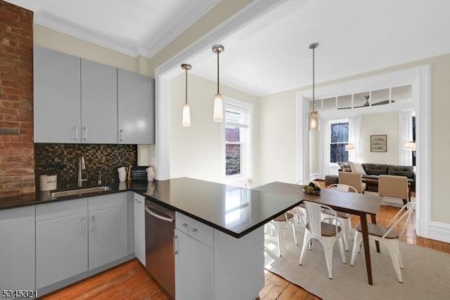 kitchen featuring stainless steel dishwasher, a sink, light wood-style flooring, dark countertops, and a peninsula