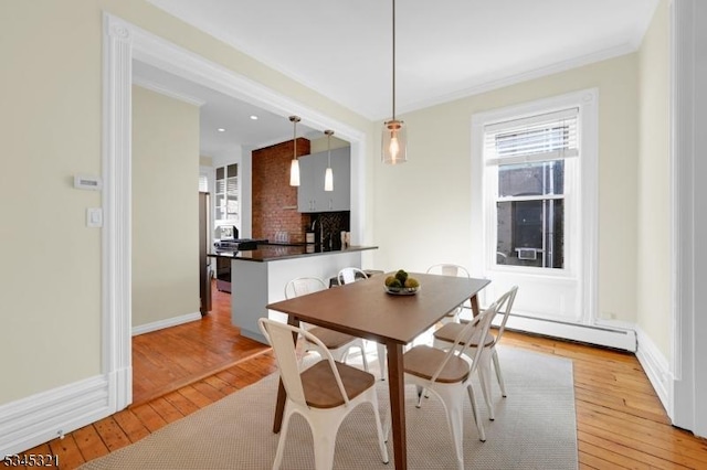 dining room featuring light wood-type flooring, a baseboard radiator, ornamental molding, and baseboards