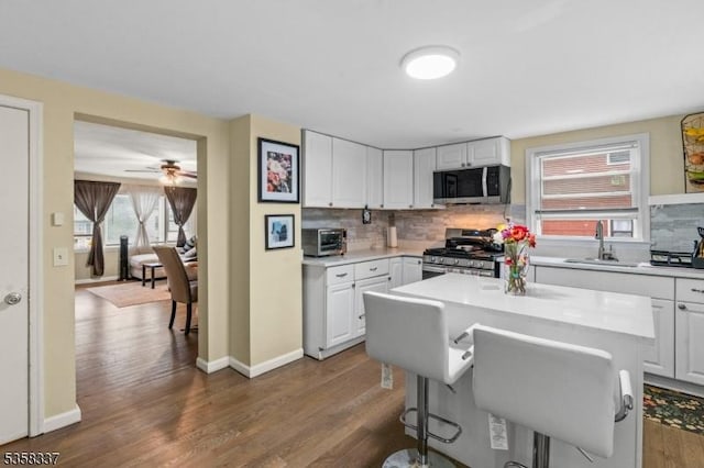 kitchen with stainless steel appliances, a sink, decorative backsplash, dark wood-style floors, and a breakfast bar area