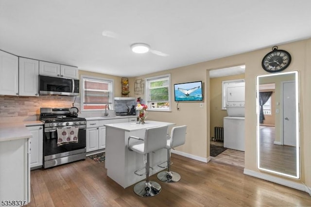 kitchen with appliances with stainless steel finishes, stacked washer / dryer, light countertops, decorative backsplash, and wood finished floors