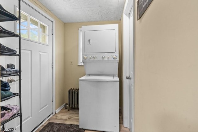 clothes washing area with stacked washer / dryer, radiator heating unit, wood finished floors, an ornate ceiling, and baseboards