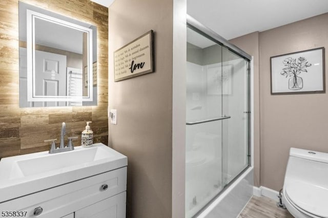 bathroom featuring toilet, vanity, wood finished floors, and shower / bath combination with glass door
