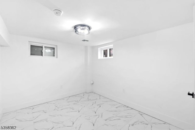 below grade area featuring light marble finish flooring and baseboards
