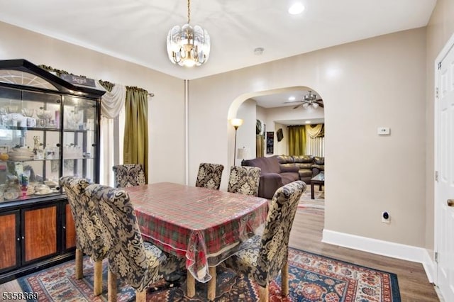 dining room with arched walkways, a chandelier, baseboards, wood finished floors, and a ceiling fan