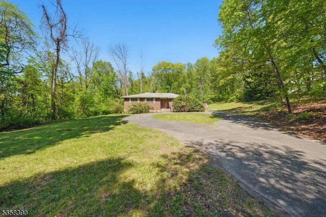 ranch-style house with a front lawn, driveway, and a forest view