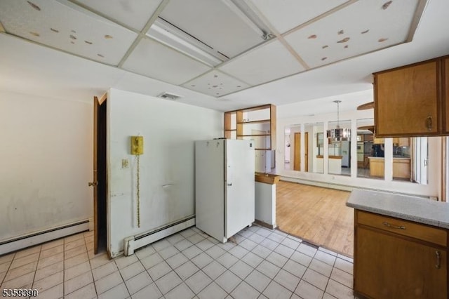 kitchen featuring baseboard heating, brown cabinetry, light countertops, and decorative light fixtures