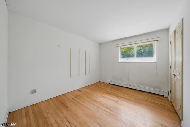 unfurnished bedroom featuring a baseboard heating unit and light wood-type flooring