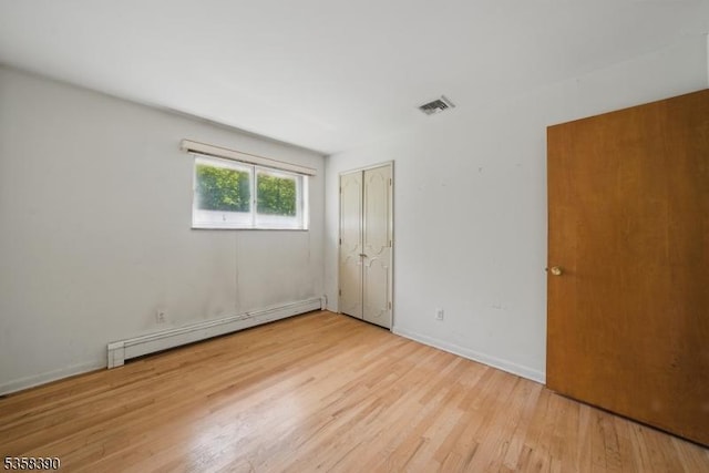 unfurnished bedroom with baseboard heating, light wood-type flooring, a closet, and baseboards
