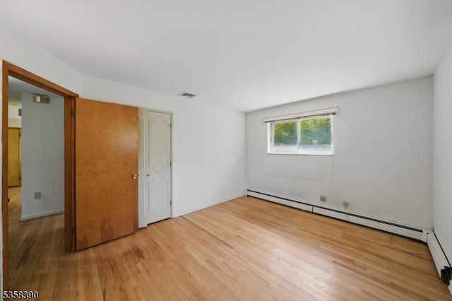 unfurnished bedroom with wood finished floors and baseboard heating