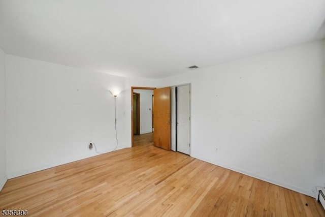 empty room with wood finished floors, baseboard heating, and baseboards