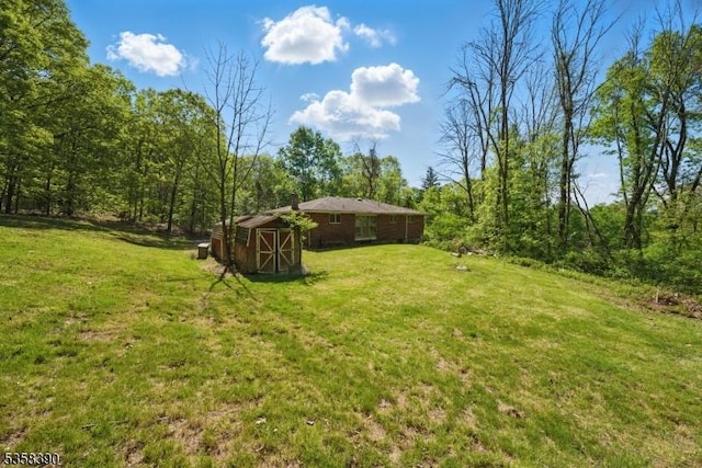 view of green lawn with an outdoor structure, a wooded view, and a storage unit