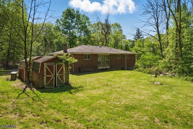 rear view of house featuring a chimney, a storage unit, a lawn, an outbuilding, and brick siding