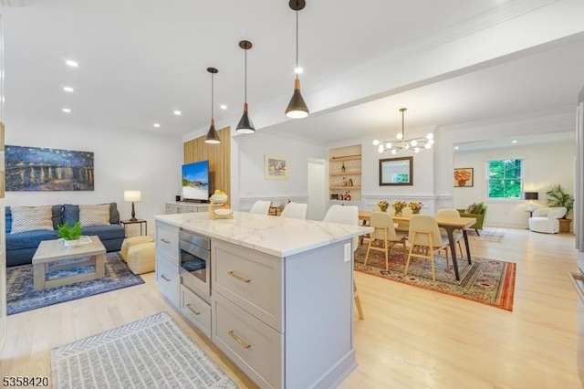 kitchen with open floor plan, ornamental molding, light wood-style flooring, stainless steel microwave, and light stone countertops