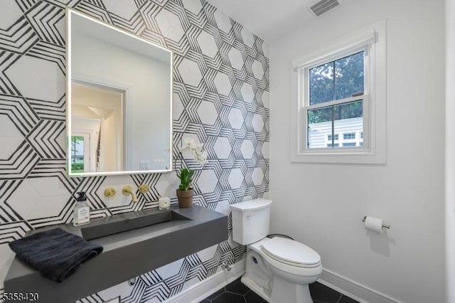 half bath with toilet, wallpapered walls, tile patterned flooring, and an accent wall